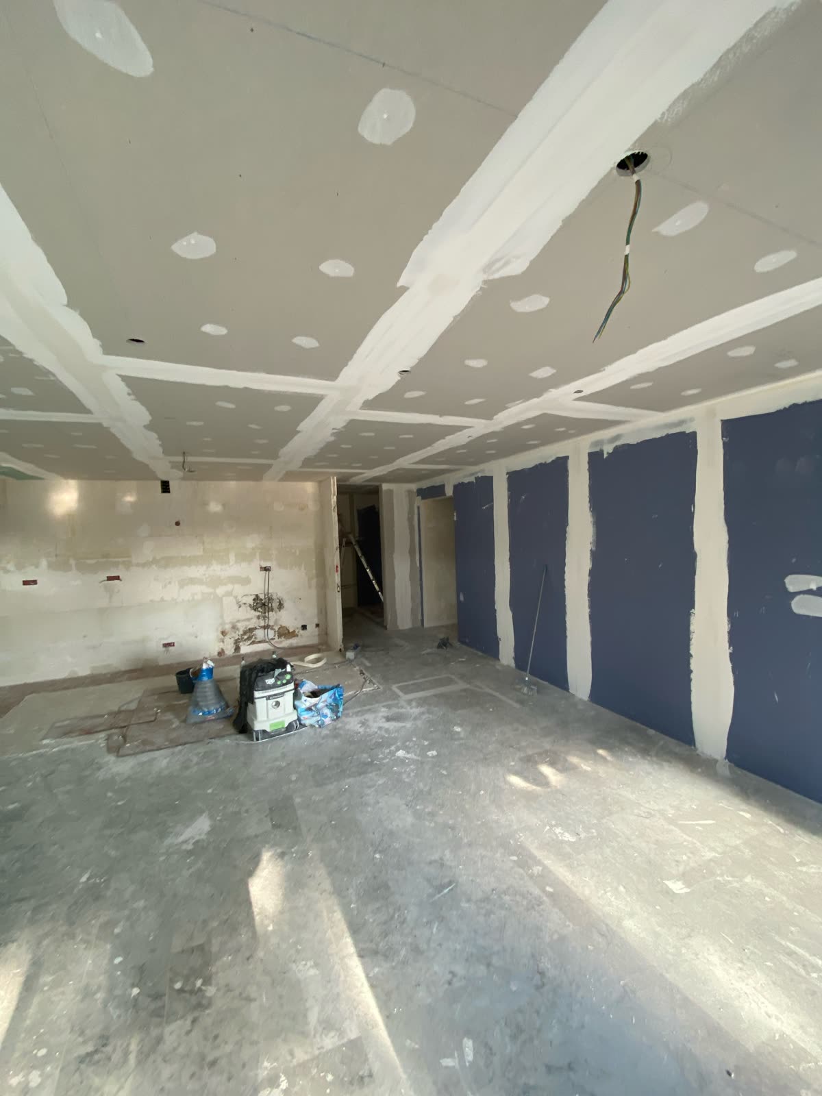 Séjour en chantier : faux plafond suspendu en plaques de plâtre avec bandes à joint et réservations de spots, et mur doublé en plaques acoustiques bleues